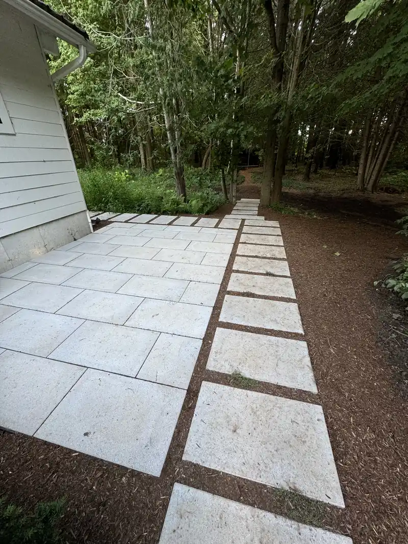 Large white stone slab patio and walkway set in mulch leading into a wooded yard