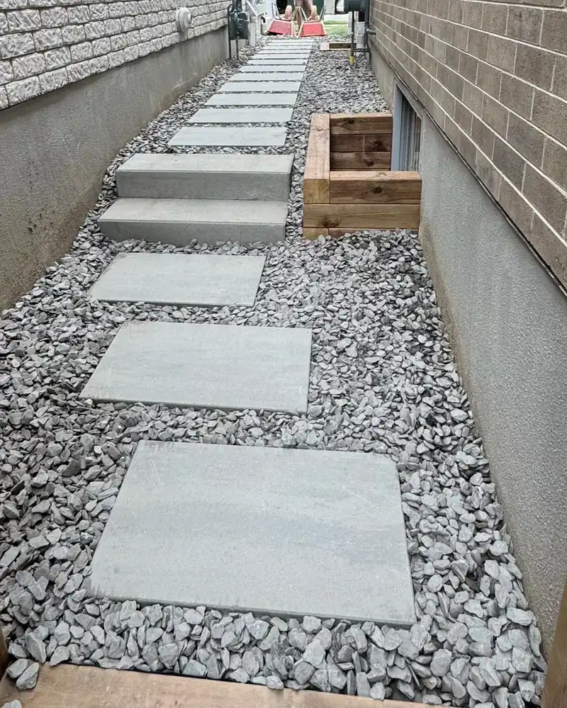 Large concrete slab walkway set in grey river stone along the side of a house